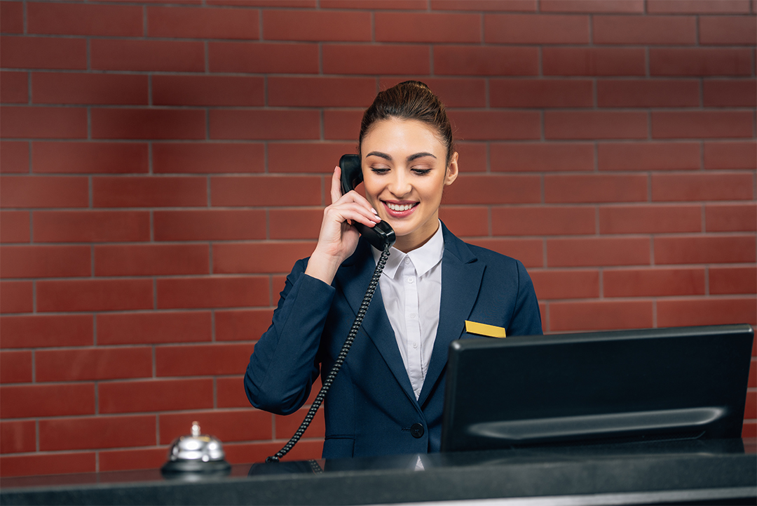 young beautiful hotel receptionist receiving call at workplace
